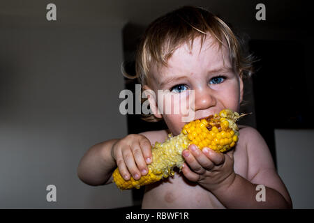 A photo of a little boy eating and enjoying maize (corn) Stock Photo