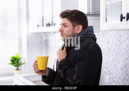Man With Scarf Around His Neck Suffering From Cold Holding Cup Of Coffee Stock Photo