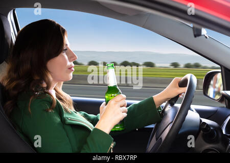 Side View Of A Beautiful Young Woman Holding Beer Bottle While Driving Car Stock Photo