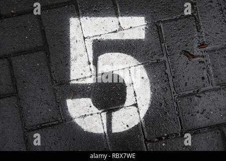 White stencil number five 5 spray painted onto dark grey paving tiles Stock Photo