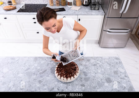 Portrait Of A Smiling Young Woman Grating Chocolate Over Cake Stock Photo