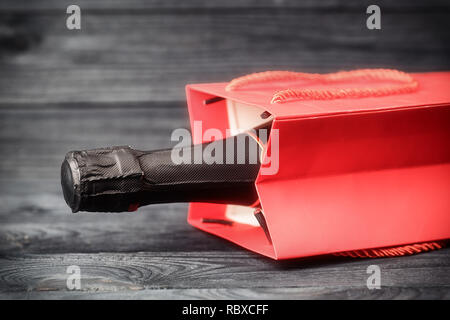 Sparkling wine in red gift bag on black wooden background. Toned image with selective focus Stock Photo
