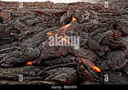 A lava flow emerges from an earth column and flows in a black volcanic landscape, in the sky shows the first daylight - Location: Hawaii, Big Island,  Stock Photo
