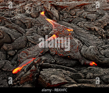 A lava flow emerges from an earth crevice and flows in a black volcanic landscape, glowing magma, first daylight - Location: Hawaii, Big Island, volca Stock Photo