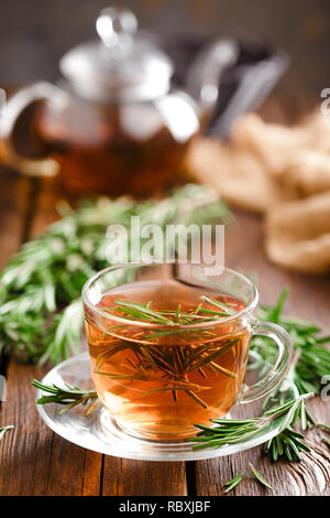 Rosemary tea in glass tea cup on rustic wooden table closeup. Herbal vitamin tea. Stock Photo