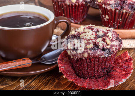 Closeup of a red velvet chocolate chip cupcake and cup of coffee on a wooden surface Stock Photo