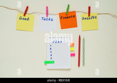 Words Goal, Tasks, Finance, Results, Plan on multicolored paper stickers with clothespins on a rope and notebook Stock Photo