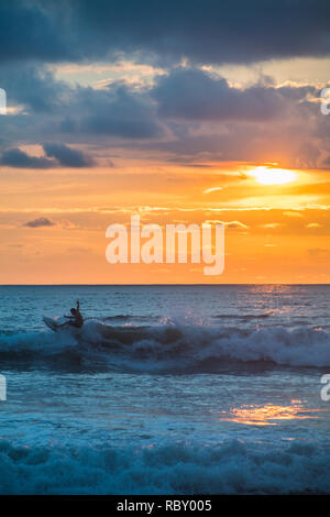 A photograph of a man surfing a wave on the background of a beautiful colorful sunset Stock Photo