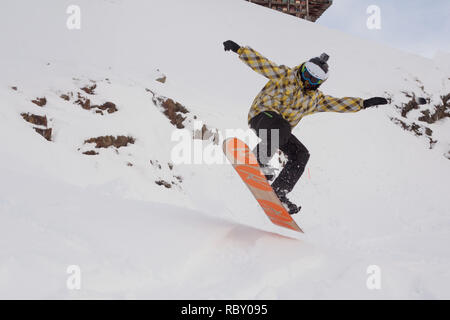 Snowboarder boy jumping into the air off slope having fun at holiday destination in French Alps. Stock Photo