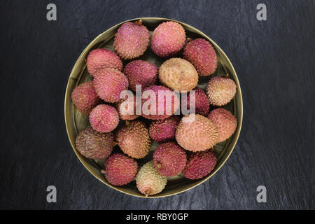 Lychees fruits in round bamboo bowl on black stone background surface with copy space Stock Photo