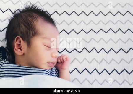 close up of cute little newborn asian baby boy sleeping on bed at children bedroom with copy space. family, healthy, life and relationship concept. Stock Photo