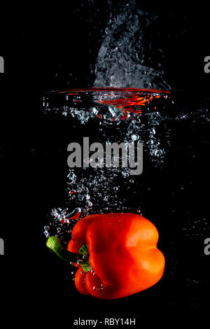 fresh organic red bell pepper or sweet pepper vegetable cleaning and drop into the water with water splash isolated on black background. Stock Photo