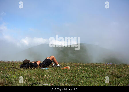 Sportive man on the mountain trek, man lies and rest. Healthy young man rests on stone having climbed up mountain top enjoy panoramic view during hike. Stock Photo