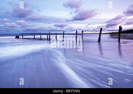Scenic view of wooden poles on a beach, the movement of the waves is shown in addition to a colorful evening sky - Location: Baltic Sea, Rügen Island Stock Photo