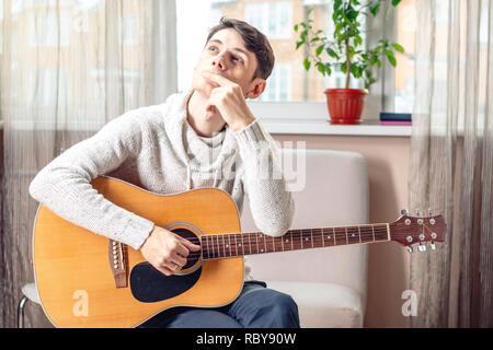 Young attractive male musician sitting on a chair holding an acoustic guitar. The concept of music as a hobby Stock Photo