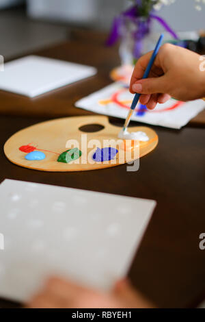 Close up colored palette with paints and blue brush in female hand. Concept of art school. Stock Photo