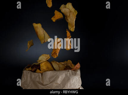 healthy chips made from vegetables or vegetable chips falling in a paper with black background Stock Photo