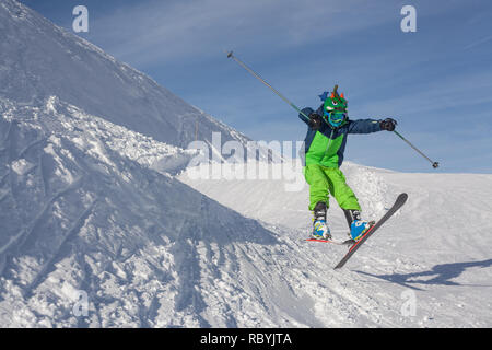 Boy ski jumping off hill in french ski resort on sunny day with blue sky. Stock Photo