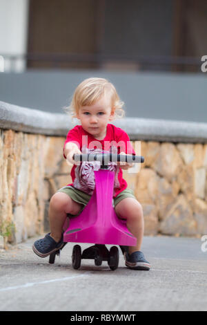 A photo of a happy kid driving with a purple plasma car like ride on toy Stock Photo