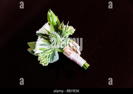 A pair of gold wedding rings and a boutonniere are next to each other on a black surface. Stock Photo