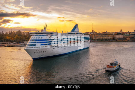 Passenger ferry and tugboat sail against Helsinki city in South Harbour at sunset, Finland Stock Photo