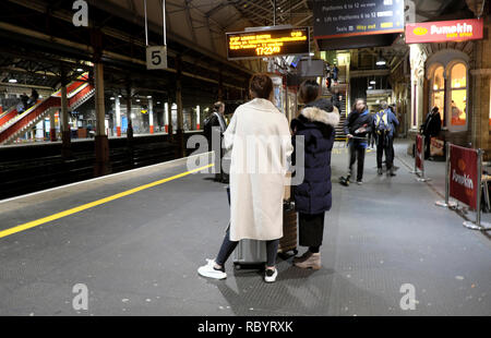 Rear view of passengers woman wearing white coat standing on platform at Crewe railway station waiting for a Virgin train to London UK    KATHY DEWITT Stock Photo