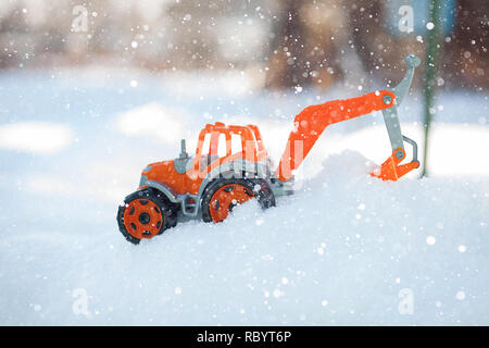 Orange toy tractor with large black wheels close-up, standing in the snow. Stock Photo