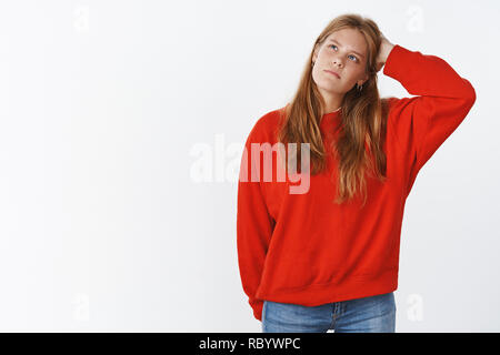 Portrait of puzzled unsure charming young female student in warm sweater standing clueless scratching head and looking at upper left corner thoughtful, thinking making decision with uncertain look Stock Photo