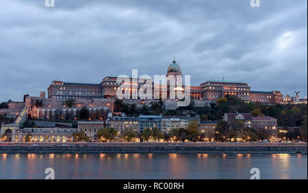 Buda Castle, overlooking the river Danube, in Budapest. It is early evening, and the castle is lit up, with the lights reflecting on the river Stock Photo
