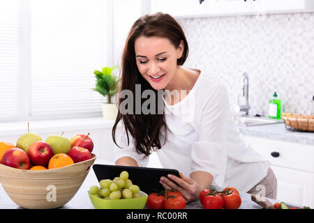 Happy Young Woman Using Digital Tablet Near Fresh Vegetables On Kitchen Counter Stock Photo