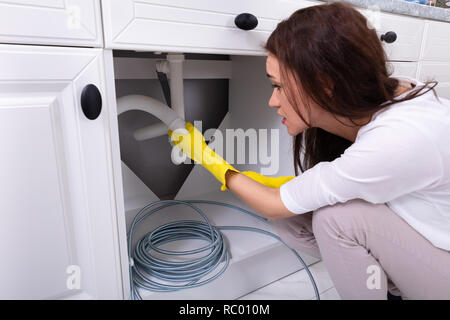 Side View Of A Young Woman Cleaning Clogged Sink Pipe In Kitchen Stock Photo