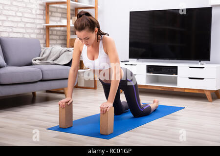 Fit Young Woman Using Wooden Blocks While Doing Exercise On Yoga Mat Stock Photo