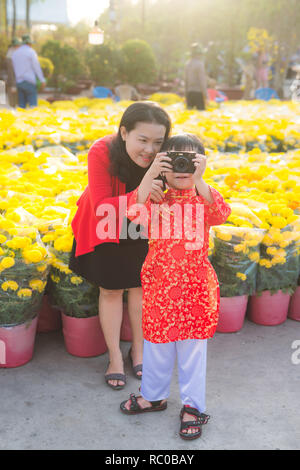 Little boy and his beautiful young mother taking picture with the digital photo camera. Happy family making photo in Tet flower market. Outdoors. Stock Photo