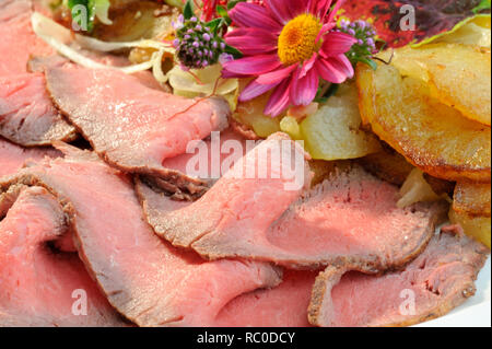 Roastbeef mit Bratkartoffeln, dekoriert mit essbaren Blüten und Kräutern | roast beef with roast or fried potatoes Stock Photo
