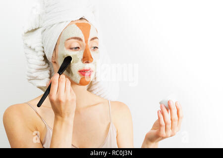 Beauty procedures skin care concept. Young woman applying facial gray and red mud clay mask to her face in bathroom. Woman with different masks on her Stock Photo