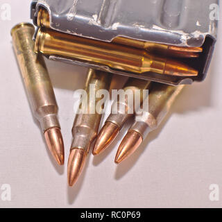 A loaded AR-15 rifle magazine on top of four .223 caliber bullets on a white background Stock Photo