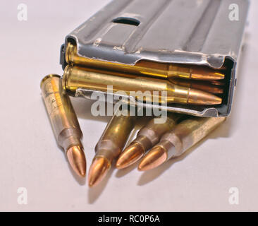 A loaded AR-15 rifle magazine on top of four .223 caliber bullets on a white background Stock Photo