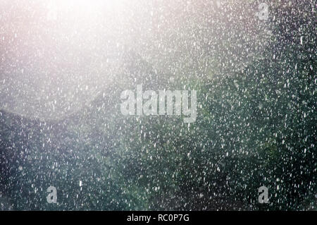 A rain shower back lit from the sun with raindrops delibrately blurred with delibrate sunflare against a dark background. Stock Photo