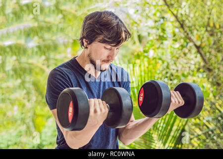 Bicep curl - weight training fitness man outside working out arms lifting dumbbells doing biceps curls. Male sports model exercising outdoors as part  Stock Photo