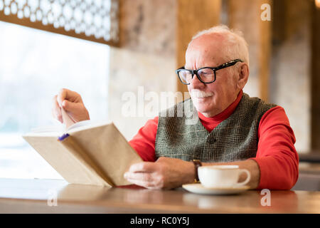 Thoughtful old man reading book in cafe Stock Photo