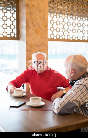 Curious senior man talking to friend in cafe Stock Photo