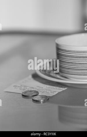 Black and white photo of coins, receipt and cup on glass table. Stock Photo