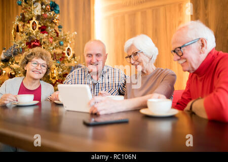 Jolly senior friends using gadget in cafe Stock Photo