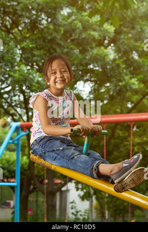 Asian girl playing on a see-saw at park. Filipina kid Stock Photo