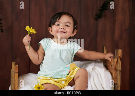 Portrait of smiling girl with yellow flower on dark wood background Stock Photo