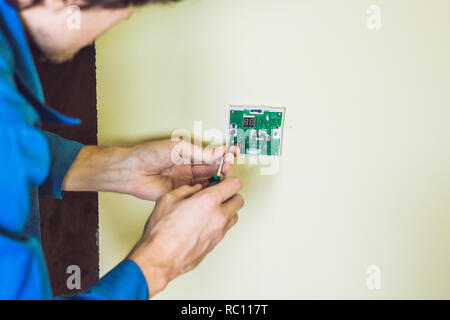 electrician installing an electrical thermostat in a new house. Stock Photo