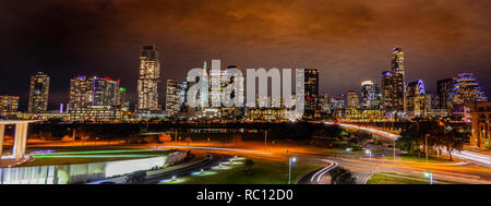 Panorama of the Austin Texas skyline at night with light illuminating architecture and cloudy sky in the background and cars streaking in foreground Stock Photo