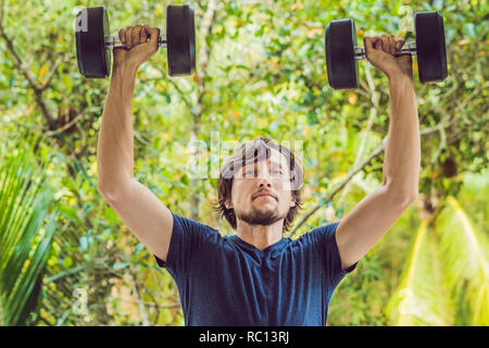 Bicep curl - weight training fitness man outside working out arms lifting dumbbells doing biceps curls. Male sports model exercising outdoors as part of healthy lifestyle Stock Photo