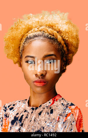 Portrait of a lovely young girl with bleached curly hair looking at camera, isolated on a peach background Stock Photo