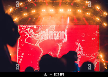 Silhouette of a big crowd at concert against a brightly lit stage. Night time rock concert with people having fun lifting hands up in the air and cheering the musicians Stock Photo